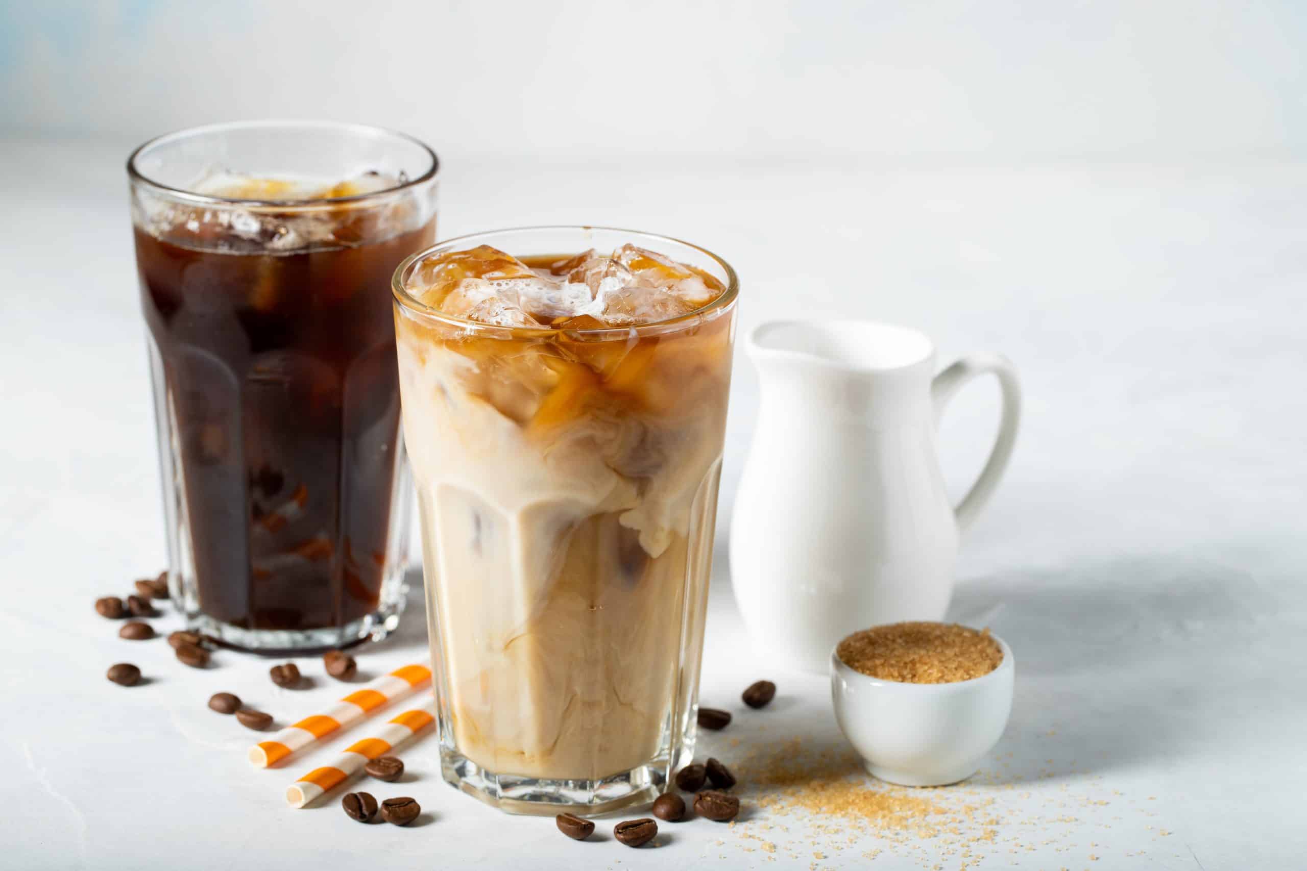 Two glasses of different colored iced coffee with a pitcher of milk.