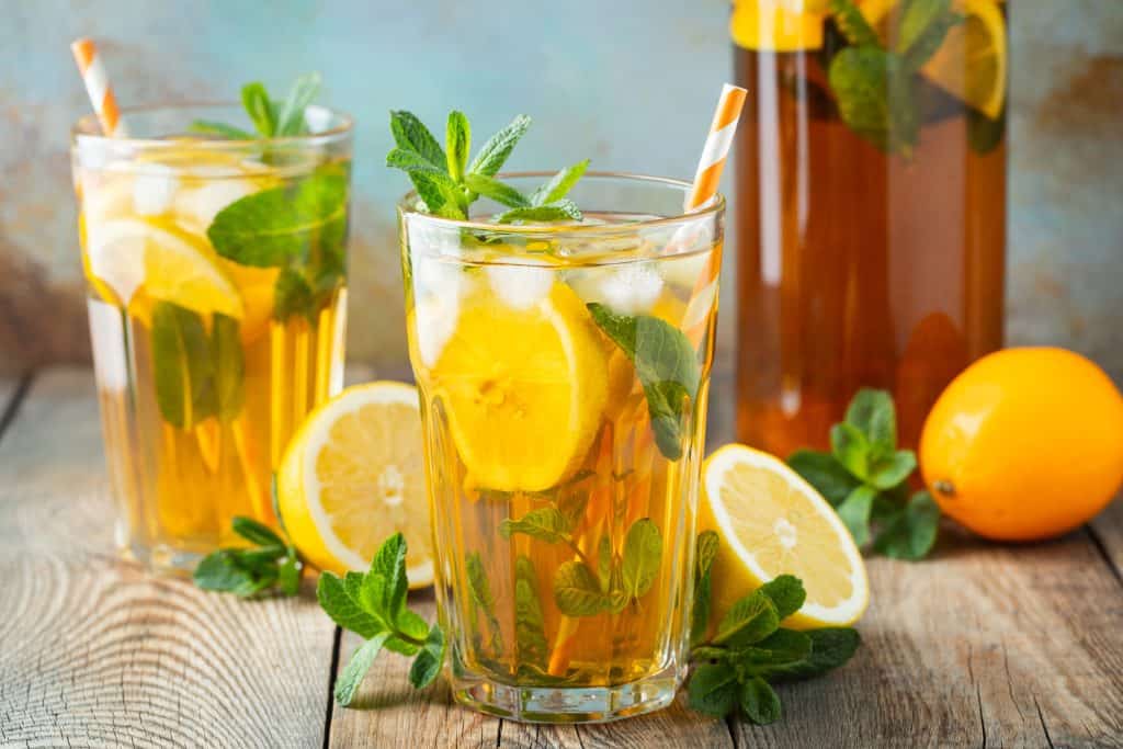 Two glasses and a pitcher of cold brew tea surrounded by lemons and mint.