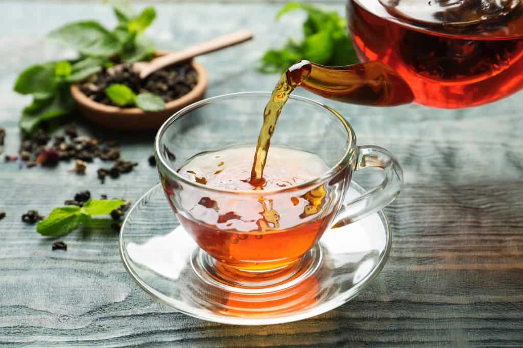 Tea being poured into a clear tea cup from a clear tea pot. 