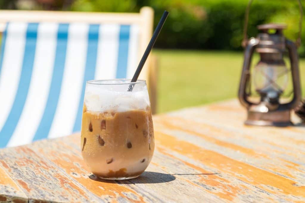 Ice coffee sitting outside on a wooden table.