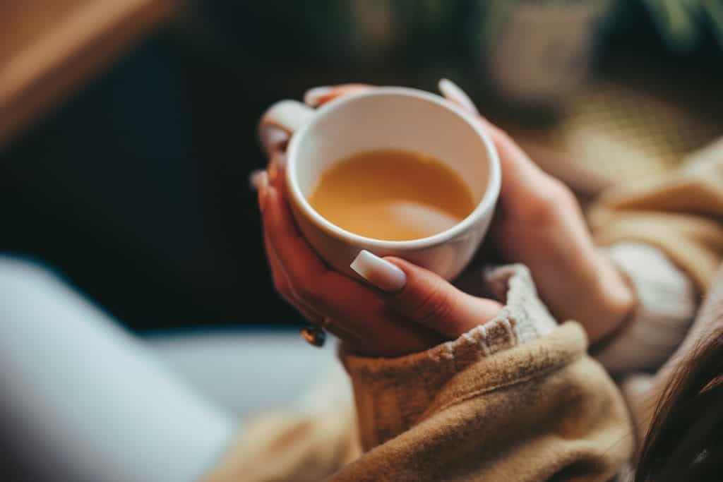 Close up of a woman holding a cup of tea in her hands.