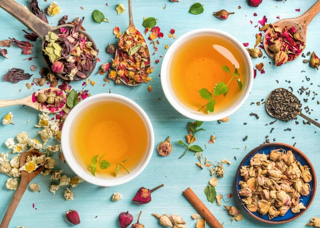 Two cups of tea surrounded by loose leaf tea in spoons. 