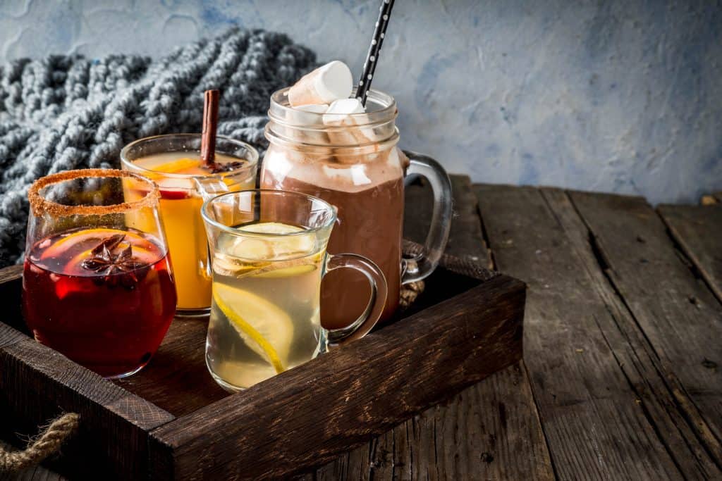 Various teas and hot chocolate drinks sitting on a wooden tray.