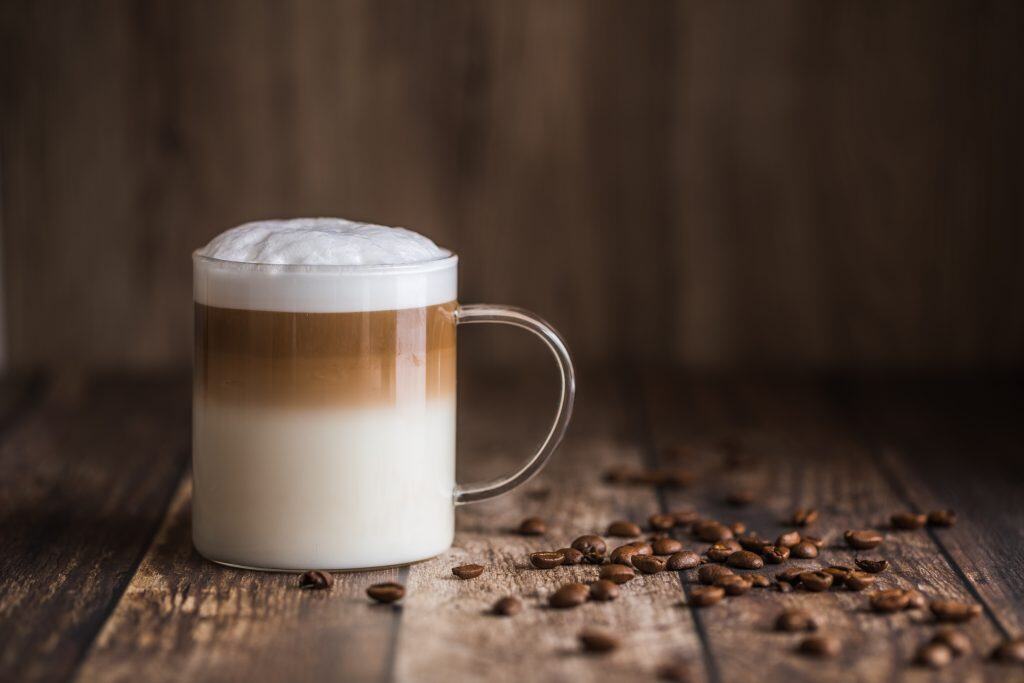 Layered latte in clear mug sitting on a wooden table.