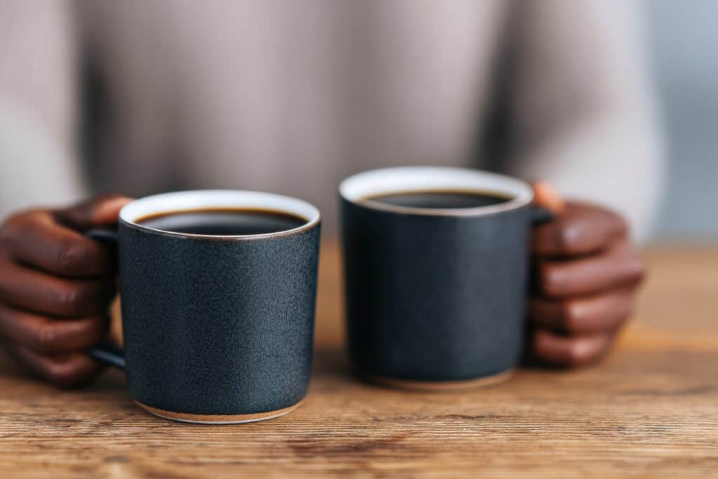 Man holding two cups of coffee on a wooden table.