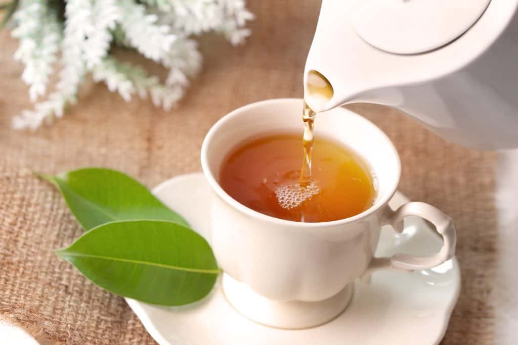 Black tea being poured into a white tea cup.