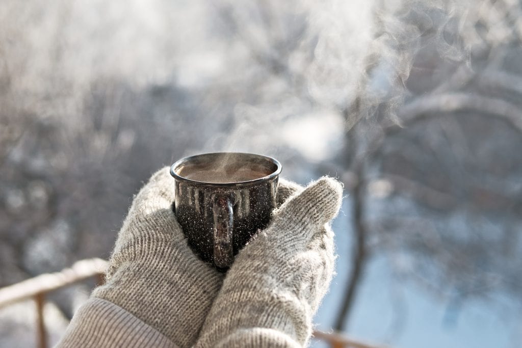 Gloved hands holding a hot cup of coffee against a winter background. 