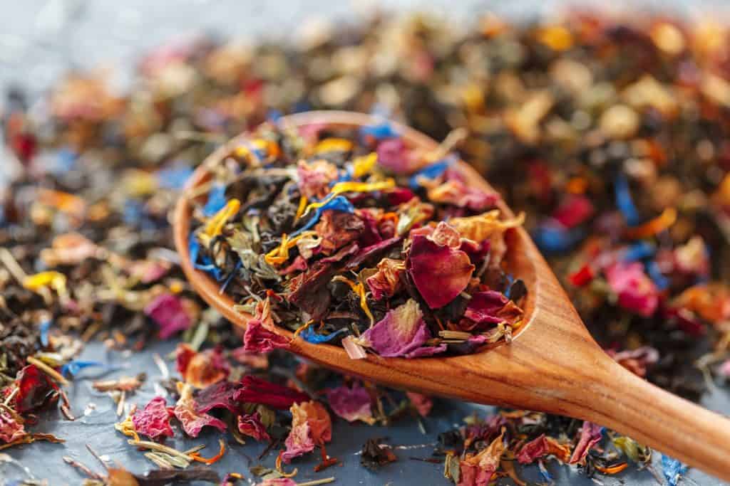 Close up of a wooden spoon holding loose leaf tea with loose leaf tea surrounding it.