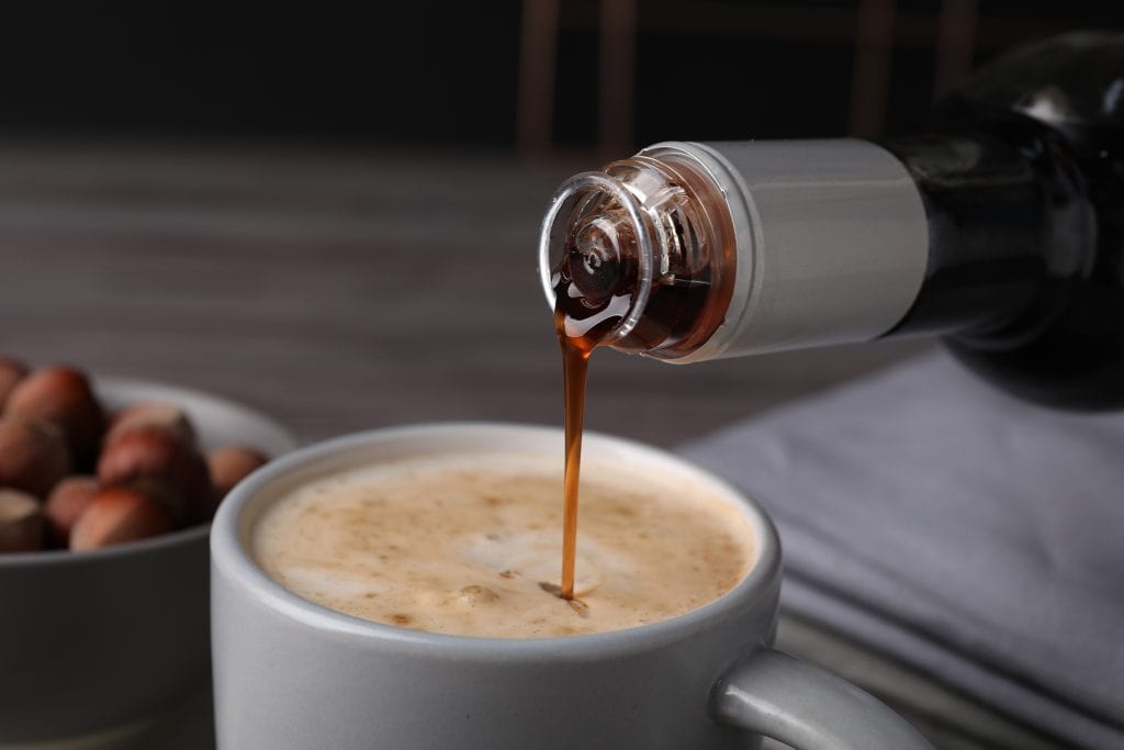 Flavored coffee syrup being poured into a cup of coffee.