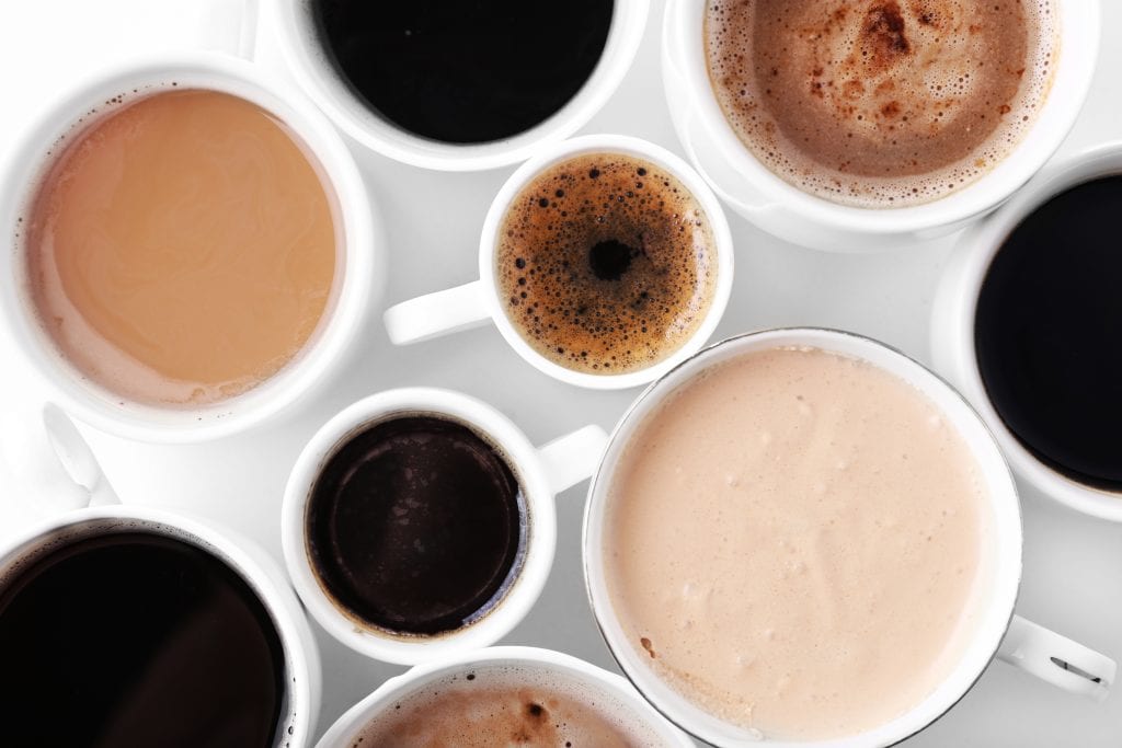 Top down view of multiple white coffee mugs with various coffees in them.