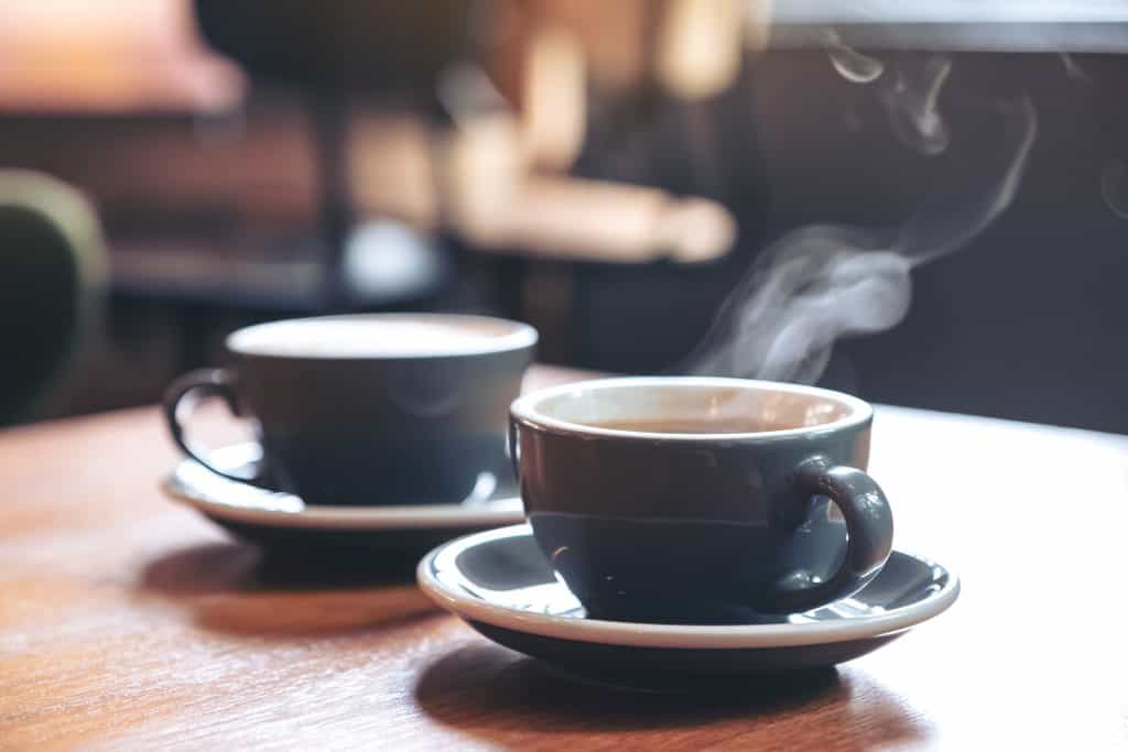 Two dark blue coffee mugs sitting on a wooden table. 