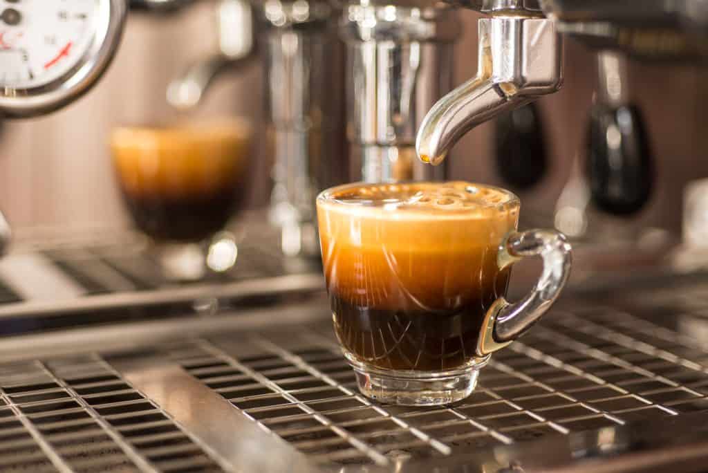 Close-up of an espresso shot in a clear espresso cup under an espresso machine nozzle.