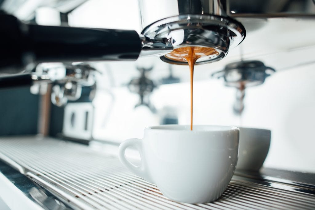 Espresso being extracted from an espresso machine into a small white cup.