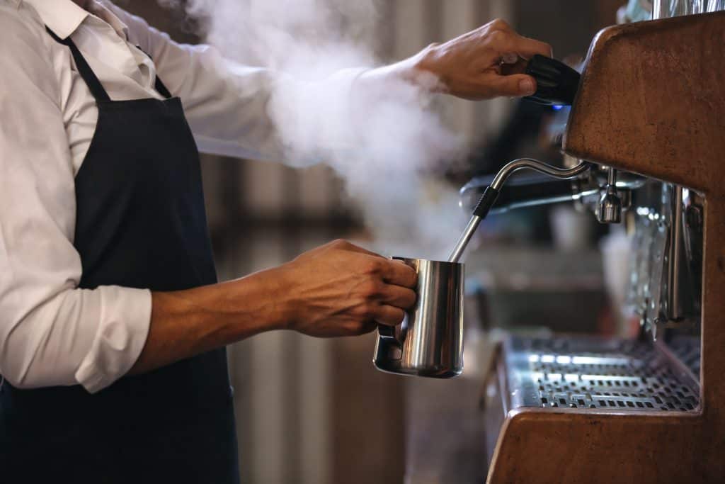 Coffee shop worker preparing coffee on steam espresso coffee machine. 