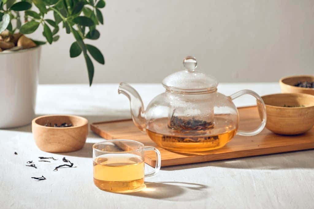 Clear teapot and tea cup on a wooden tray with amber colored tea inside. 