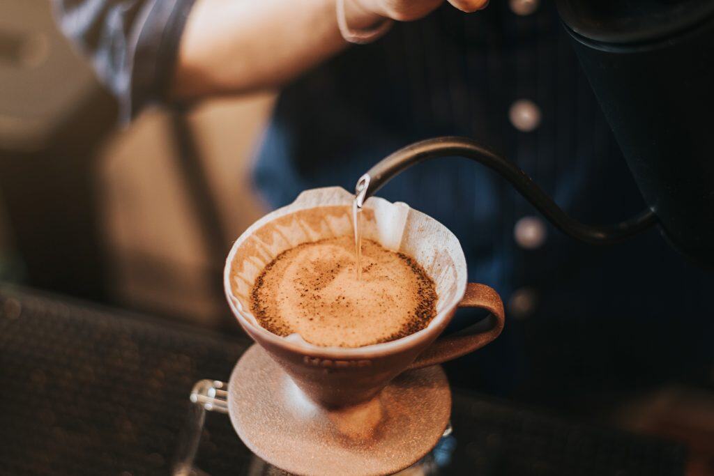 Barista pouring hot water into coffee grounds in a pour-over coffee vessel.