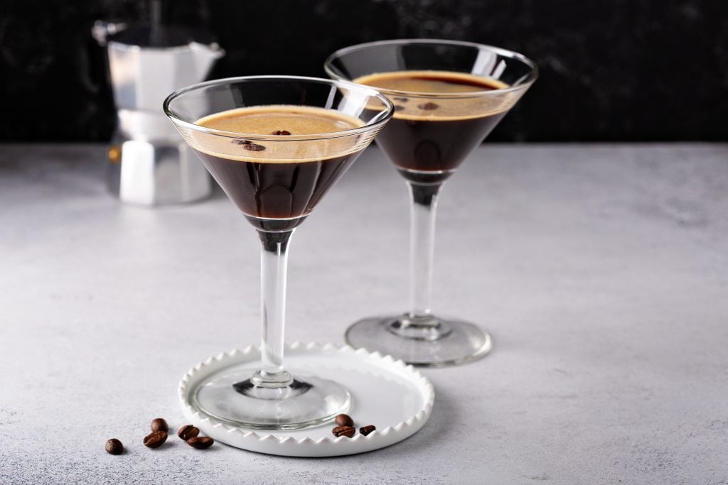 Two espresso martinis sitting on a white marble counter with                                                                                                                                                                                                                        a moka pot in the background.