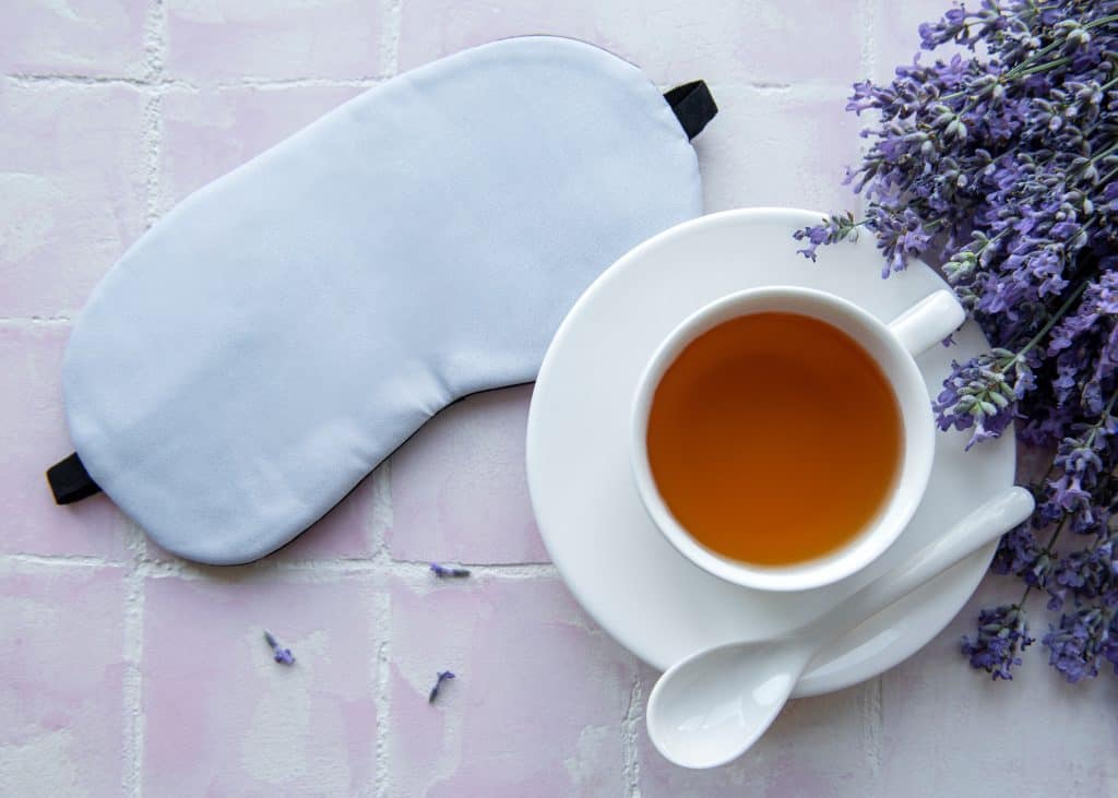 White teacup on a tiled background with lavender and a sleeping eye mask.